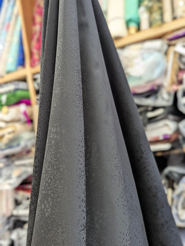 Black fabric with a textured starry pattern draped in a fabric store setting