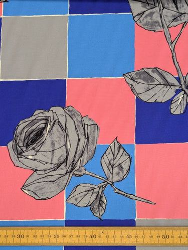 Fabric with grey roses on a checkered pattern of blue, pink, and grey squares, with a ruler shown at the bottom for scale.