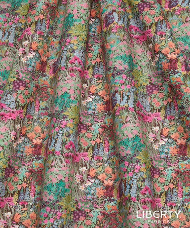 A close-up of Liberty Fabrice floral fabric with a dense, multicolored pattern of pink, orange, green, blue, and purple flowers on a muted sage background.