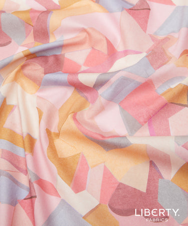 A close-up of draped Liberty Fabrics featuring a pastel geometric pattern with pink, peach, yellow, and light gray shapes.