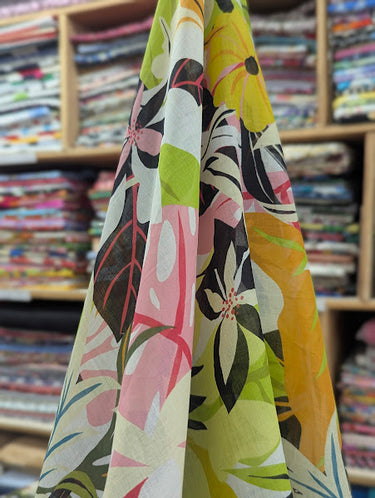 Printed pure cotton fabric with a colourful tropical pattern in pinks, greens, and yellows draped within a shop setting.