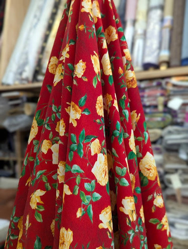 Close-up of a printed wool fabric with yellow flowers on a red background, shown draped over a table within a store setting.