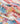 A close-up of a lightweight fabric with a colorful coastal print in a mix of pink, blue, yellow, red, and white tones, and laid in soft folds.