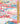 A close-up of a colorful printed fabric pattern showing a stylized landscape with pink, blue, white, yellow, and red hills, houses, trees, and clouds, with a ruler standing vertically on the right side for scale.