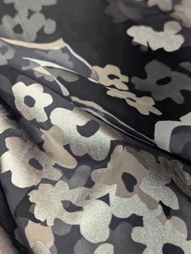 Close-up of a silk chiffon fabric with a foil printed floral design in champagne, silver and grey on a black base.