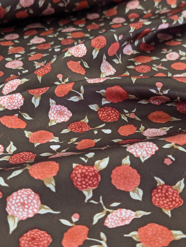 A close up view of silk satin fabric with a floral pattern in shades of red and copper on a brown background.