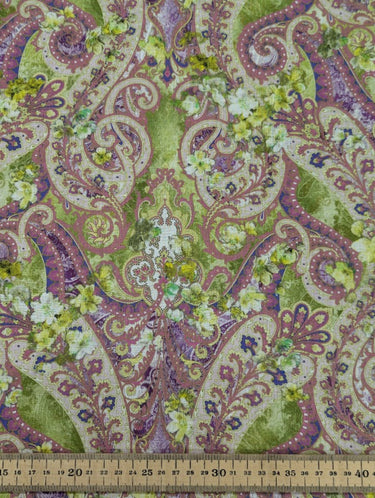 A linen fabric with an intricate paisley pattern in warm, earthy tones of muted greens, purples, and pinks, accented by floral motifs, and a ruler shown for scale.