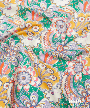 A close-up of Liberty Fabrics floral print fabric featuring a retro paisley and floral pattern in green, yellow, orange, white, and purple.