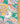A close-up of a colorful paisley and floral patterned fabric with a wooden ruler on the right side for scale. The design features yellow, orange, pink, purple, and white motifs on a bright green background, with a Liberty London watermark in the bottom right corner.