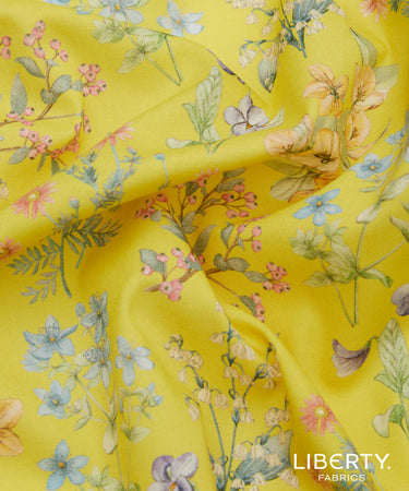 Yellow Liberty Fabrics floral print fabric with delicate watercolor-style flowers and leaves in pink, blue, green, and peach tones, shown with soft folds.