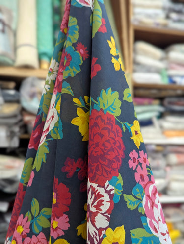 Floral fabric with red, yellow, and blue flowers on a dark background, displayed in a store setting.