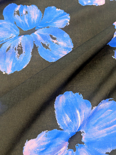 Close-up of printed pure cotton fabric, with floral patterns in blue and lilac on a black base.