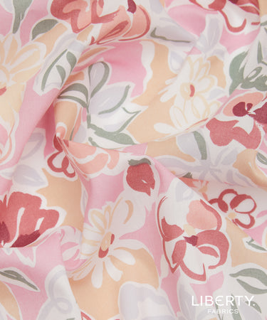 A close-up of draped fabric with a soft floral print in pastel pink, peach, white, coral, and muted green. The Liberty Fabrics logo is visible in the bottom right corner.