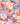 A close-up of a Liberty brand fabric pattern featuring a colorful floral design on a coral red background with white, blue, yellow, and green elements.