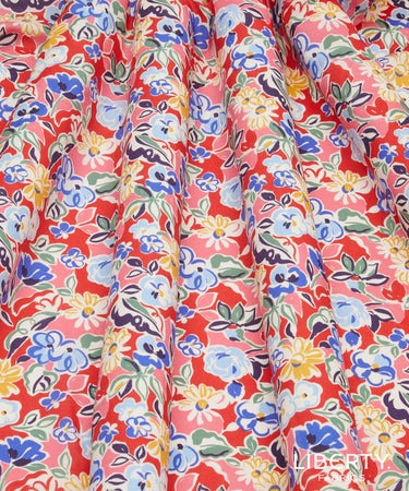 A close-up of a draped fabric with a dense floral print. The pattern features blue, yellow, and white flowers with green leaves on a bright coral-red background.