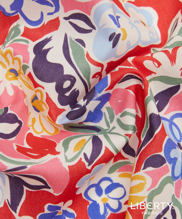 A close-up of draped Liberty Fabrics featuring a vibrant floral pattern with red, pink, blue, purple, green, and yellow motifs on a white base.