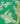A close-up of a green patterned fabric or wallpaper featuring a vintage paisley and floral design in yellow, white, and light blue, with a wooden ruler standing vertically on the right side for scale.