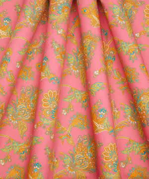 Pink fabric with a dense floral and paisley pattern in yellow, teal, and orange, shown with soft folds.