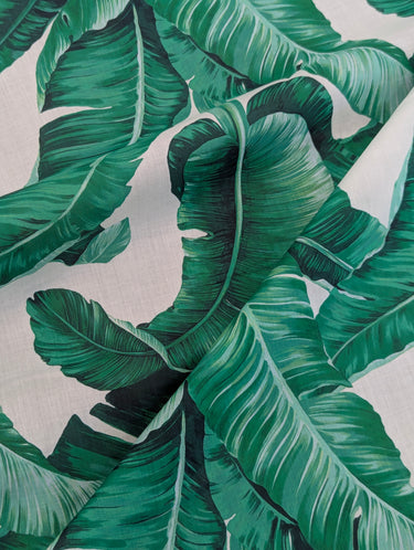 Close-up of a fine printed cotton lawn fabric with green banana leaves on a white background