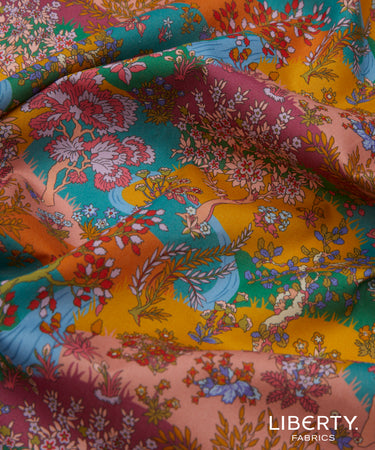 A close-up of draped Liberty Fabrics featuring a vibrant, multicolor floral and botanical print with a deer motif. The print showcases a rich palette of teal, mustard yellow, dusty pink, burgundy, and orange, with the 'LIBERTY.