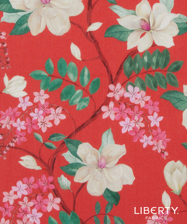 A close-up of a Liberty Fabrics floral pattern featuring cream magnolia flowers, pink blossoms, and green leaves on a vibrant red background.