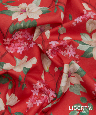 A close-up of draped Liberty Fabrics featuring a red floral pattern with pink blossoms, cream-colored magnolia flowers, and green leaves.