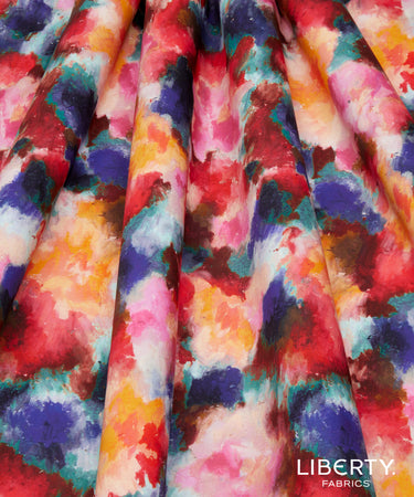 A close-up of draped fabric with a vibrant watercolor-style abstract print in red, pink, orange, yellow, teal, blue, purple, and white.