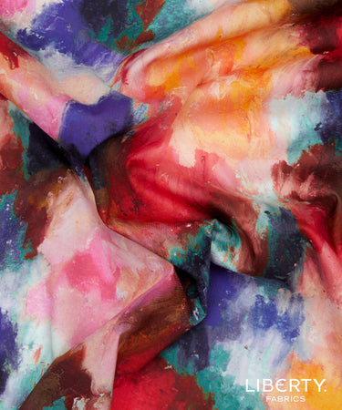 A close-up of draped Liberty Fabrics featuring a vibrant, painterly abstract pattern with blended shades of red, pink, purple, teal, orange, and white.