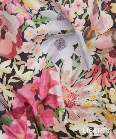 A close-up of a Liberty Fabrics floral fabric with a dense watercolor-style print featuring pink, white, yellow, and green flowers on a dark background.