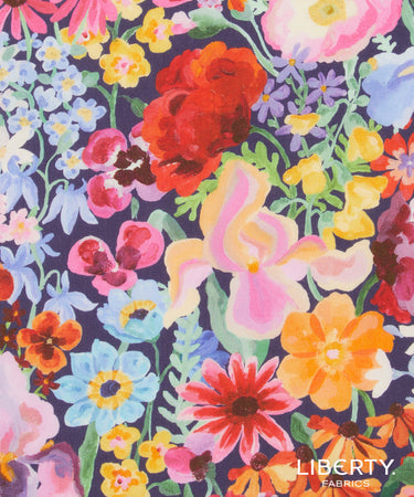 A close-up of a colorful floral fabric pattern with large and small watercolor-style flowers in pink, red, yellow, blue, orange, and purple on a dark navy background.