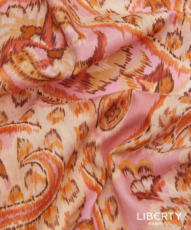 A close-up of draped Liberty Fabrics featuring a pink, orange, and beige ikat pattern.