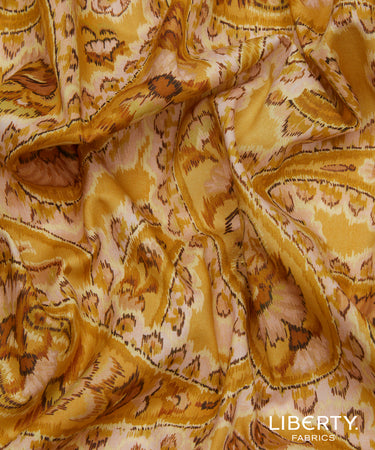 A close-up of draped Liberty Fabrics featuring a golden yellow and beige ikat pattern with brown accents.