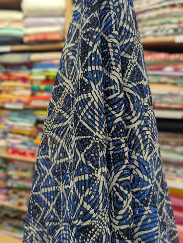 A printed pure cotton batiste, with a geometric motif in cobalt blue, ivory, and black, with interlocking circles and angular lines, shown draped within a shop setting.