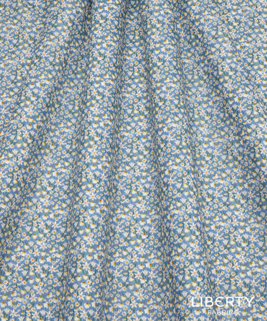A close-up of Liberty Fabrics' 'Daisy' pattern, featuring a dense floral print of small white daisies with yellow centers on a dusty light blue background.