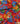 A close-up of a red fabric with a vibrant floral print featuring blue, yellow, and orange flowers with green leaves. The fabric is draped to show its texture and pattern, with a 'LIBERTY FABRICS' logo in the bottom right corner.