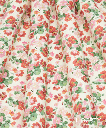 A close-up of a pleated fabric with an all-over floral print in shades of pink, red, orange, and green on a cream background. The Liberty Paris logo is visible in the bottom right corner.