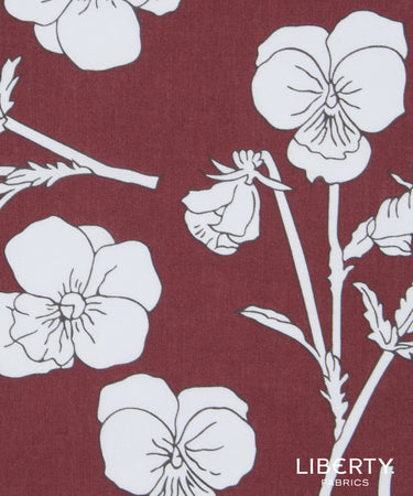 A close-up of Liberty Fabrics floral fabric featuring white pansy flowers and stems printed on a deep burgundy background.