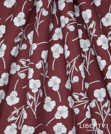 A close-up of a fabric with a dark reddish-brown background and a white floral line-art pattern. The fabric is draped to show its texture and print.