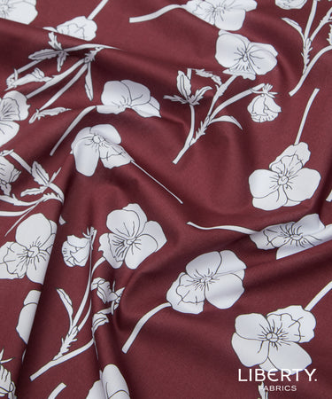 A close-up of draped Liberty Fabrics featuring a deep burgundy red satin-like fabric with a white floral print.