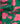 A close-up of green fabric with a bright pink floral print, featuring large flowers and buds with the text 'LIBERTY. FABRICS' in the bottom right corner.