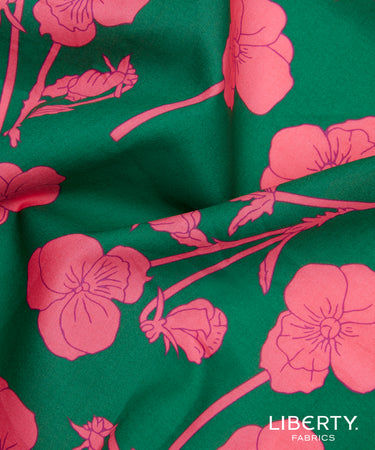 A close-up of green fabric with a bright pink floral print, featuring large flowers and buds with the text 'LIBERTY. FABRICS' in the bottom right corner.