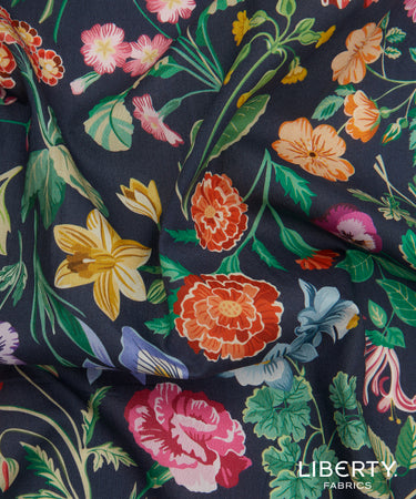 A close-up of Liberty Fabrics floral print fabric with a dark navy background and colorful flowers including pink, orange, yellow, and blue blossoms with green leaves.