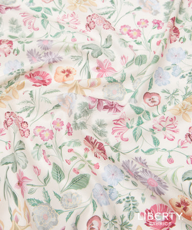 A close-up of a lightweight fabric with a delicate, multi-colored floral print on a warm cream background. The pattern features pink, red, purple, and blue flowers with green leaves.