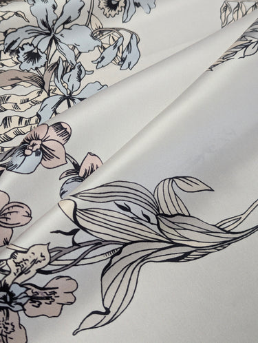 A close up of Silvene 100% Silk Satin fabric with a floral pattern in a grey, blue and white colour range, showing the material's sheen and weave.