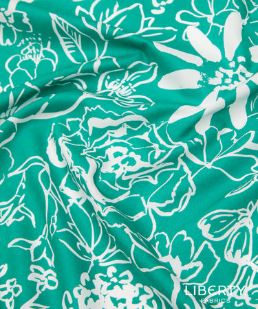 A close-up of a teal green fabric with a white floral line-art pattern, showing soft folds and a visible Liberty Fabrics logo in the bottom right corner.