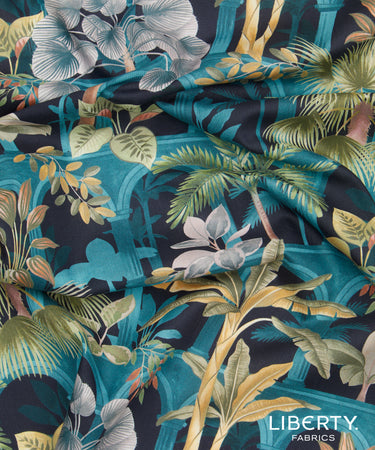 A close-up of draped Liberty Fabrics featuring a tropical botanical print with palm trees, monstera leaves, and blue flowers on a dark navy background with teal arches.