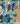 A close-up of a tropical fabric pattern featuring palm trees, banana leaves, and arches in teal, navy, and gold, with a gold metal ruler on the right side and a 'Liberty Fabrics' logo in the bottom right corner.