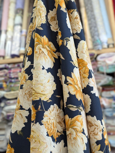 Photo of a printed pure wool fabric featuring yellow flowers on a navy background, draped within a shop setting.