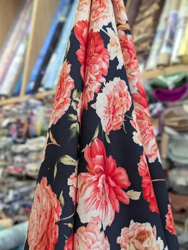 Printed pure wool fabric with pink and red flowers on a dark navy background, displayed within a store setting.