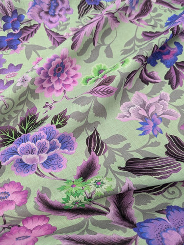 A linen fabric with a bold floral print featuring primarily blue, pink and grey colours on a green background.